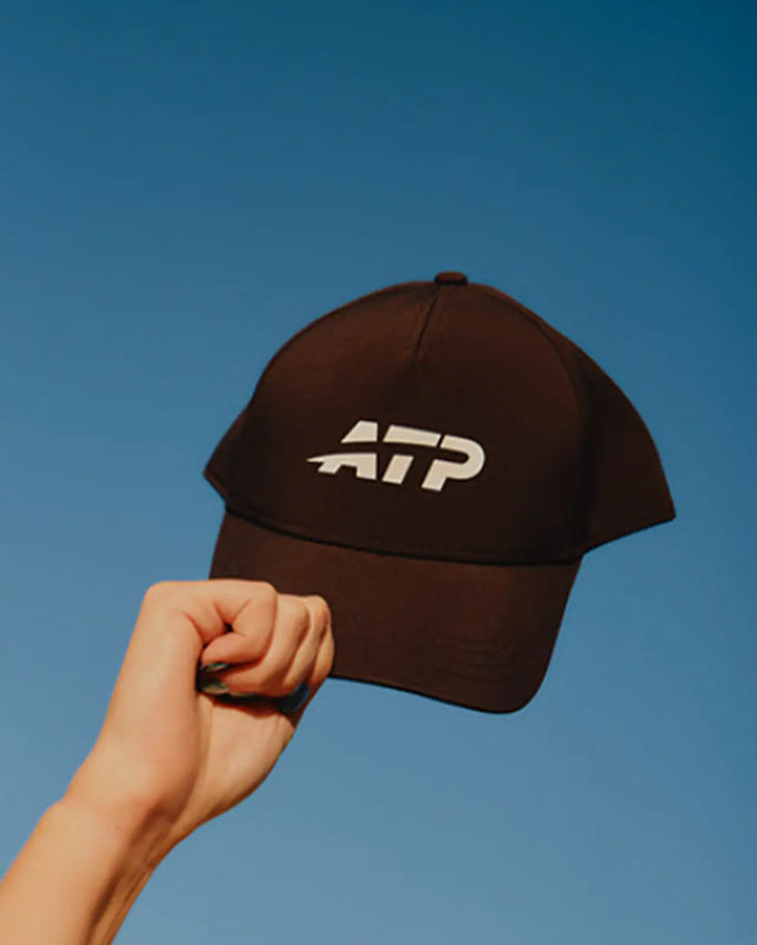 Black cap with ATP logo held against a clear blue sky