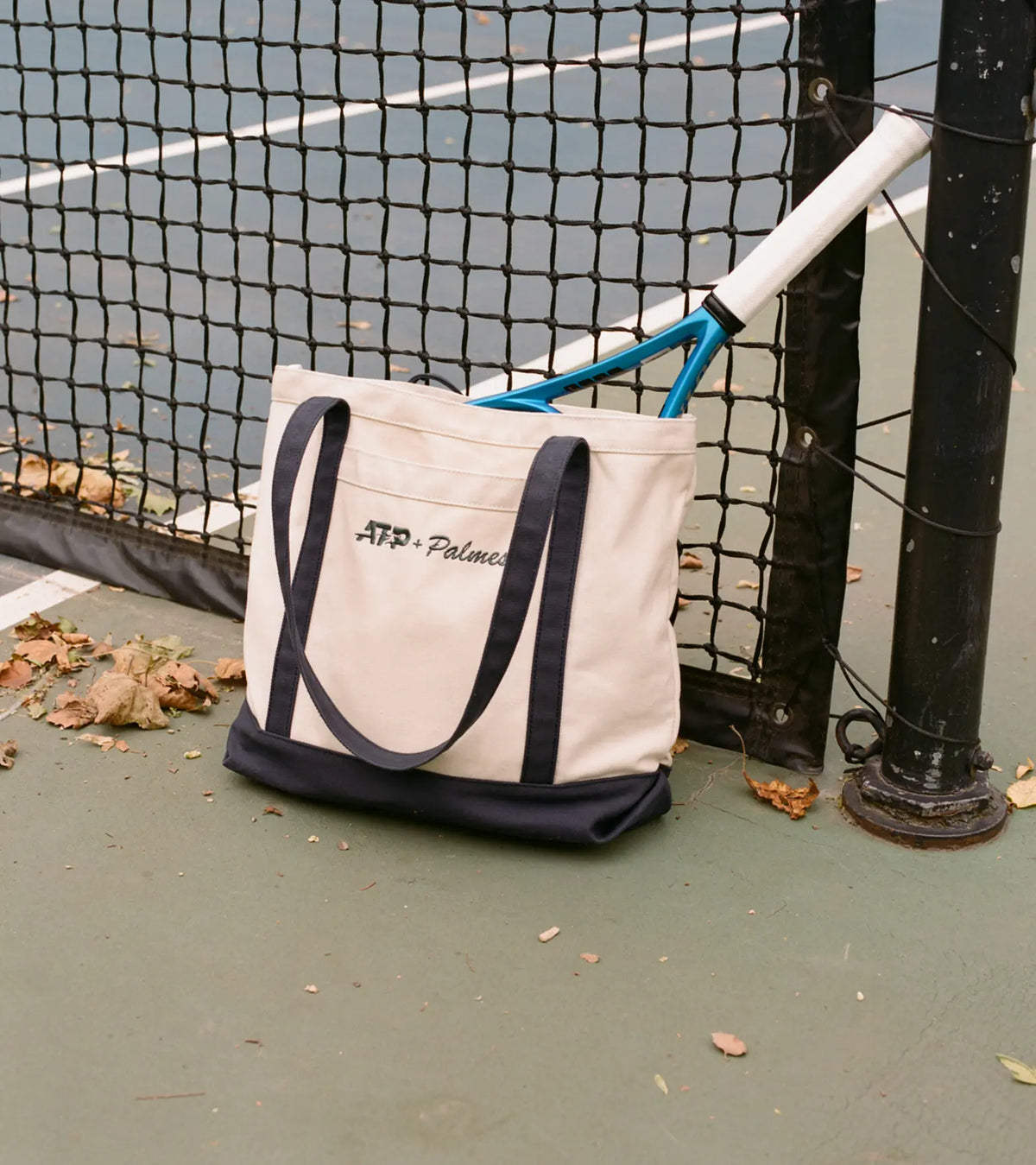 Tote bag with a Palmes logo on a tennis court carrying a racket
