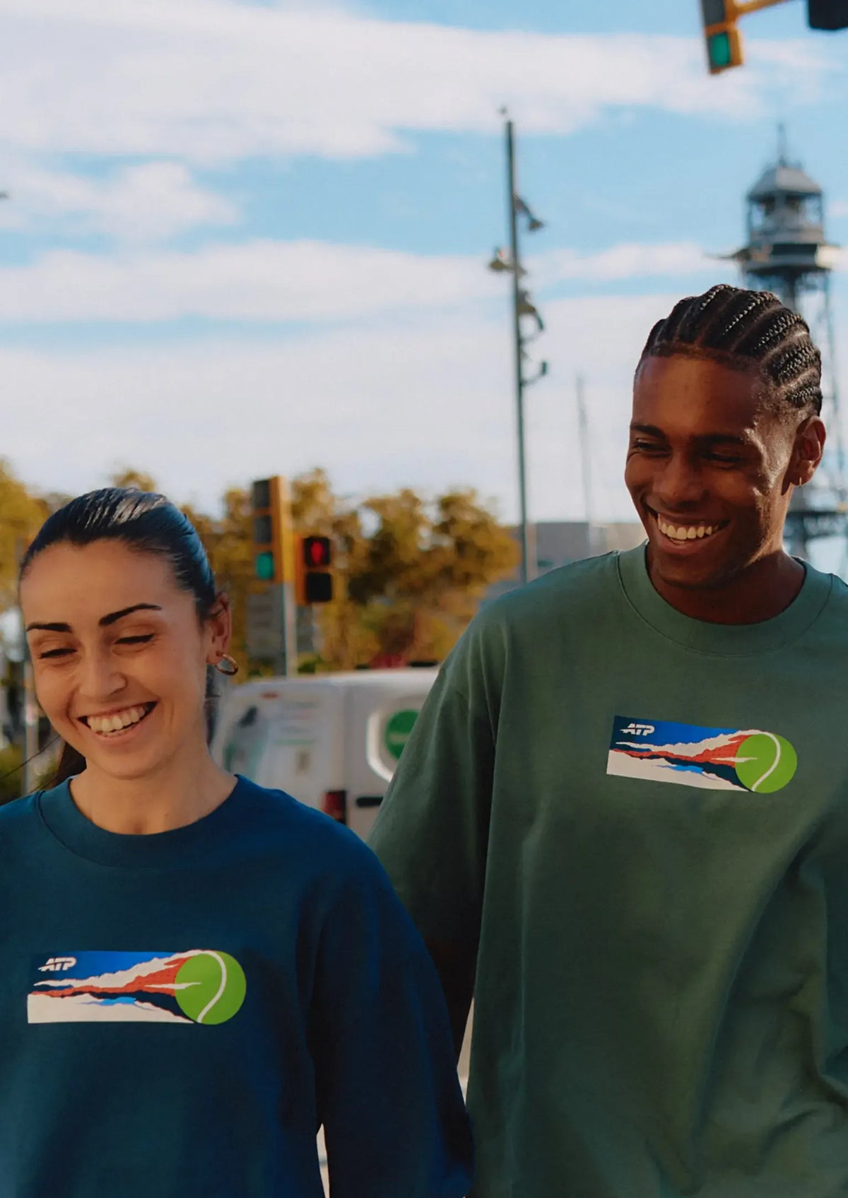 Two people wearing ATP clothing standing together outdoors with a clear sky and urban background.