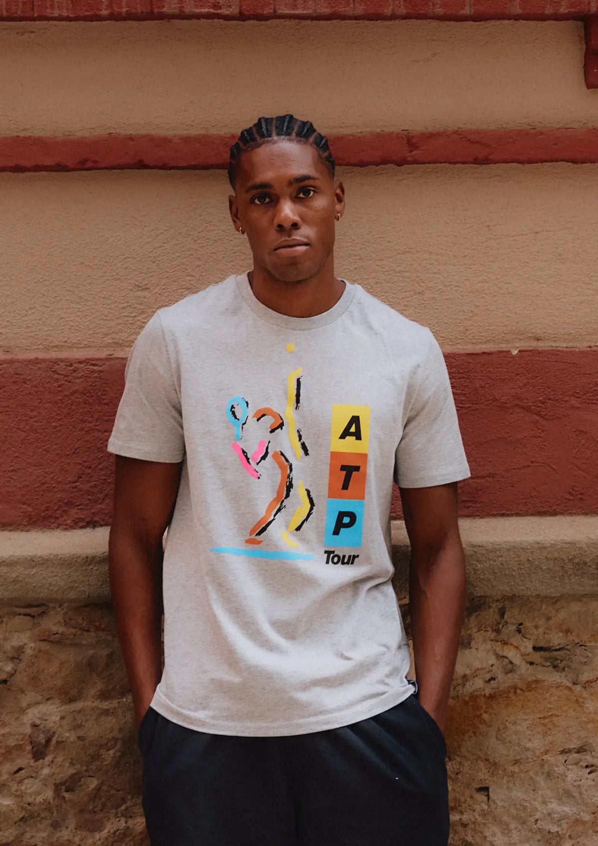 Person wearing a white t-shirt with colorful graphics against a textured wall.