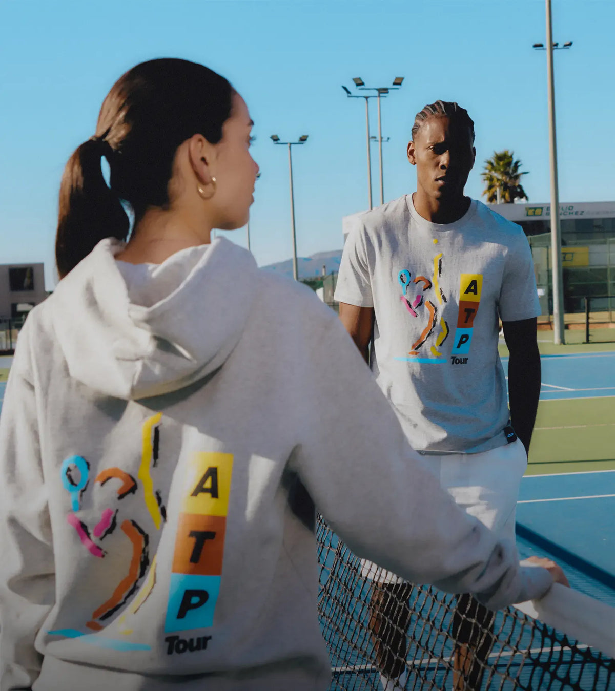 Two people on a tennis court wearing ATP Tour shirts.