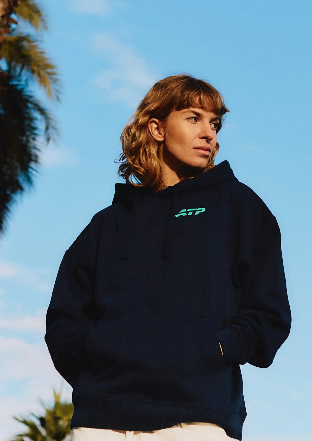 Woman wearing a black hoodie with an ATP logo against a blue sky
