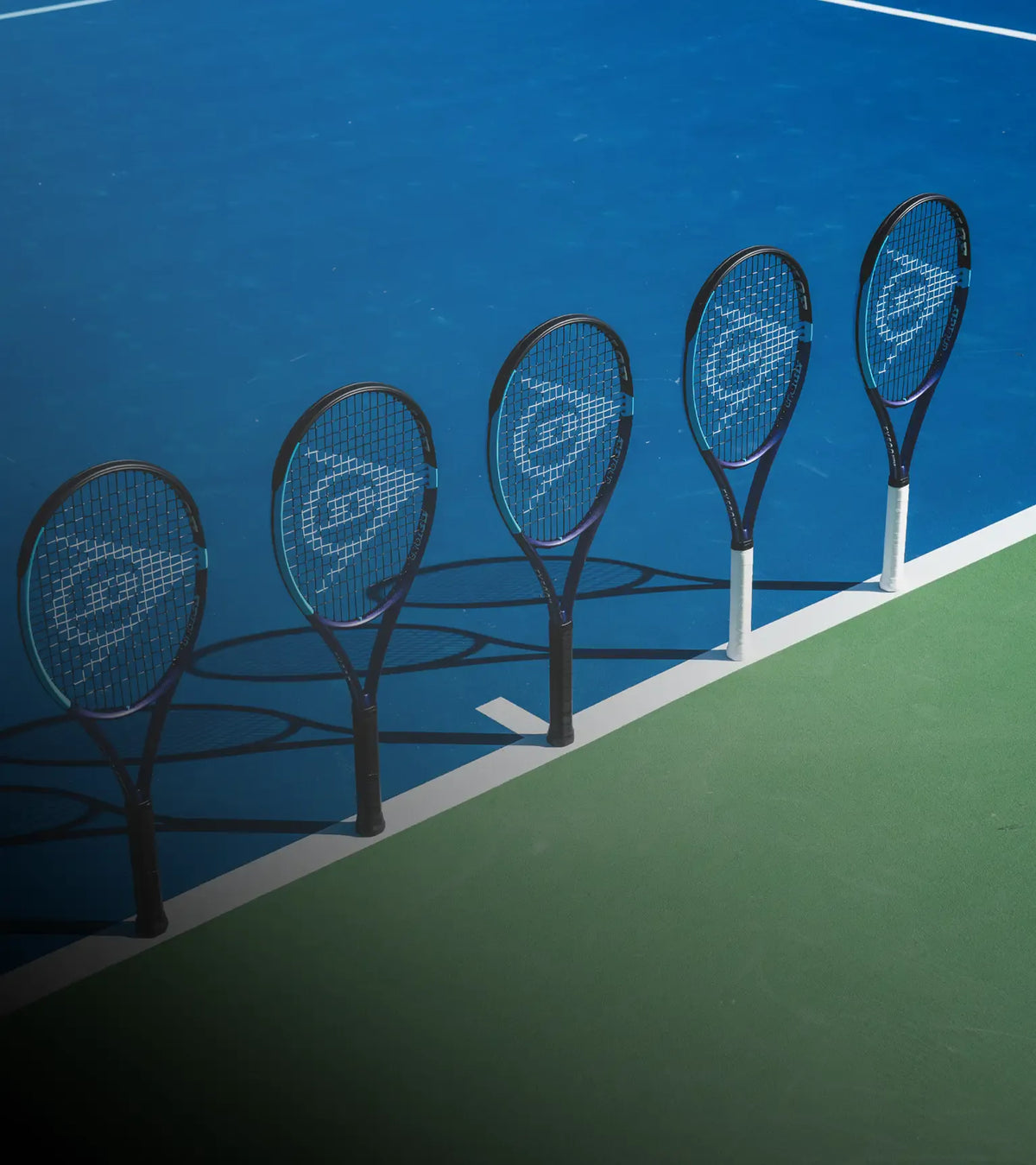 Five tennis rackets lined up on a tennis court with blue and green colors.