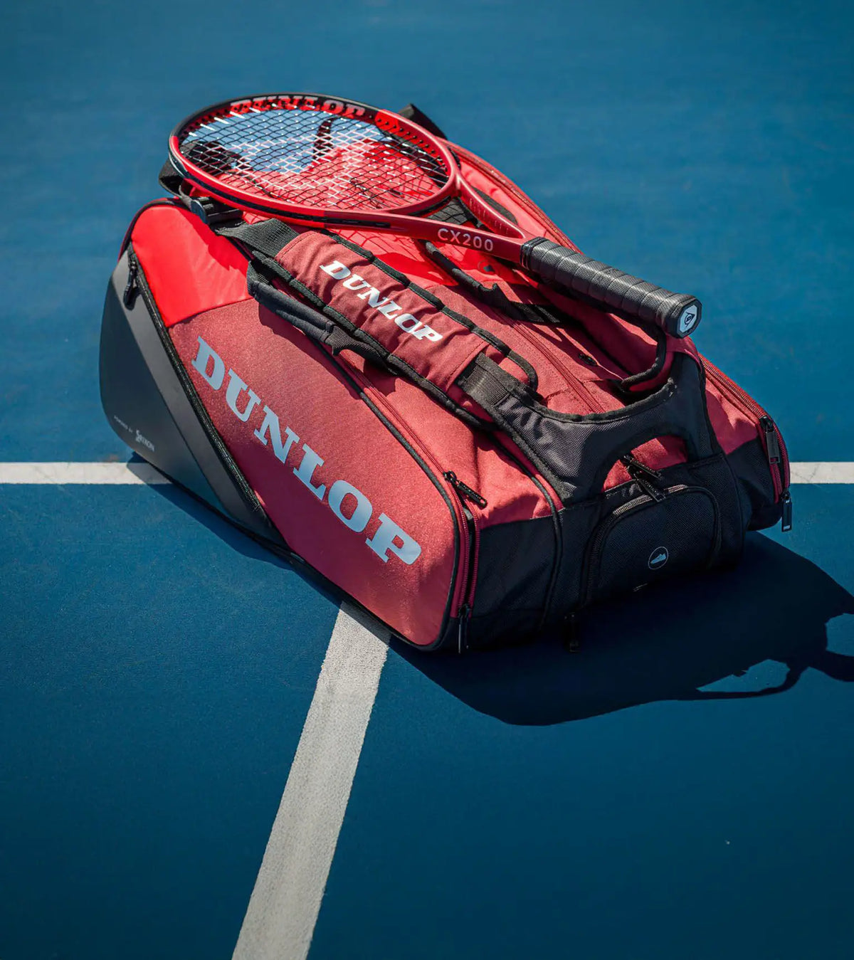 Red Dunlop tennis racket bag with a racket on a blue tennis court