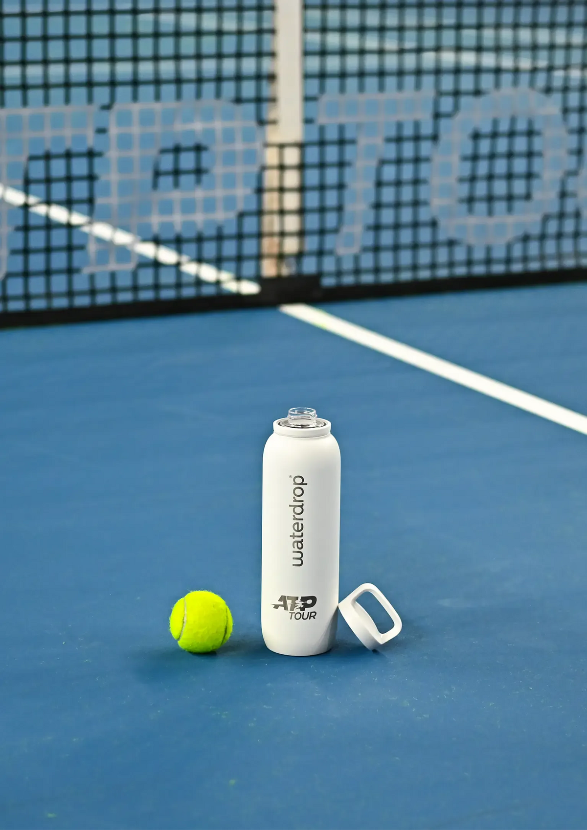 Waterdrop Water Bottle on a blue tennis court next to a tennis ball