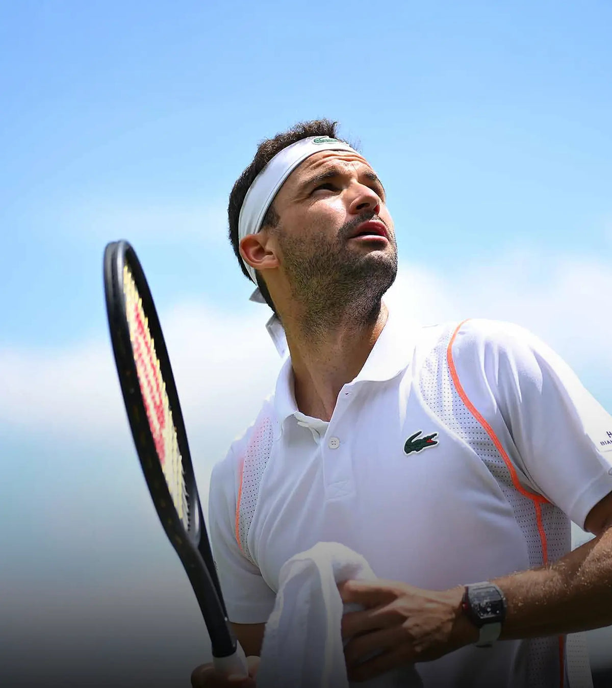 Grigor Dimitrov in action on a tennis court with a clear blue sky.